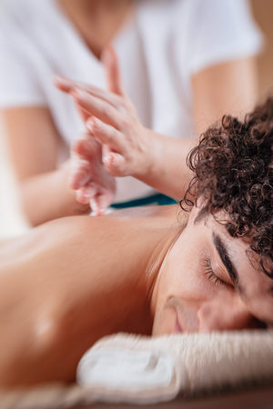 Close-up of handsome healthy young man enjoying relaxing back massage at beauty salon. Selective focus.の写真素材