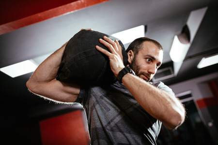 Strong man doing cross training with sandbag at the gym.の写真素材