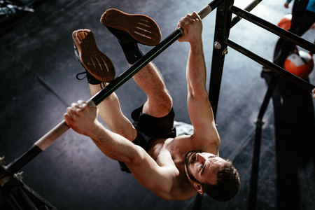 Strong young muscular man doing toes to bar exercise at the gym. の写真素材
