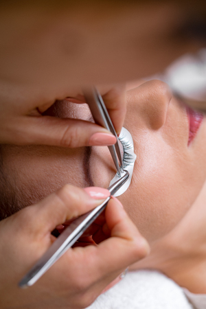 Close-up of a beautician hands applying extended eyelashes to model.  の写真素材