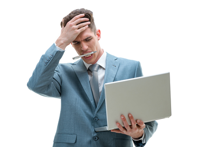 Young upset businessman holding laptop in the hand, checking document and worried about business problem, depressed by bad news, isolated on white background. の写真素材