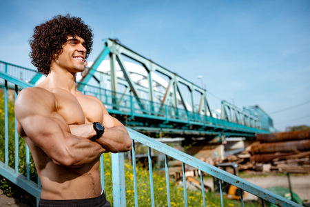 Strong bodybuilder with crossed arms and naked torso with six pack, perfect ABS, shoulders, biceps, triceps and chest standing on bridge steps, ready for morning workout. の写真素材