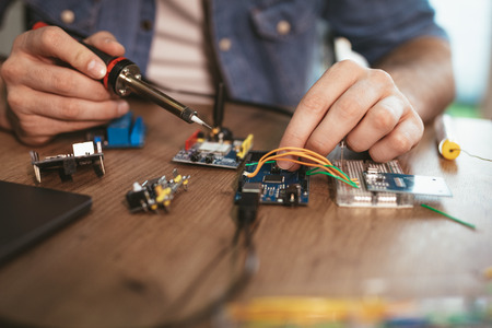 Close-up of a male hands soldering circuit board by soldering iron on the table.