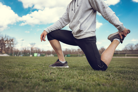 Close-up of a unrecognizable active young man stretching and doing exercises in the public place, on empty stadium.の写真素材