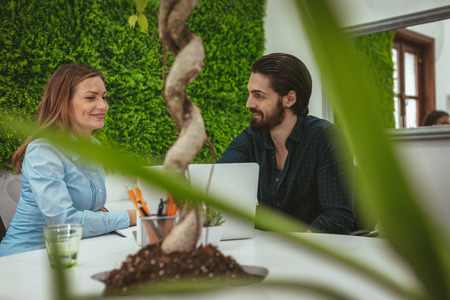 Young successful designers talking about project at the office. Young woman listens her colleague and records the facts in the notebook.の写真素材