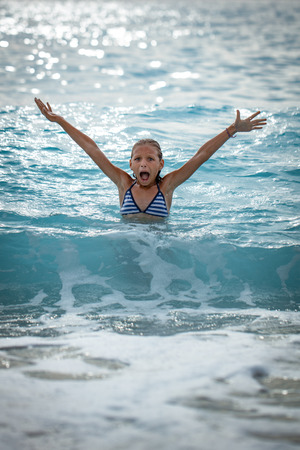 A little girl having fun in the waves of the sea and the drops of water are splashing all over her.の写真素材