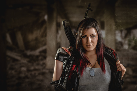 Attractive dark-haired girl in camouflage shirt hold machine gun leaning on the shoulder and with a dangerous expression on her face looking at the camera.の写真素材