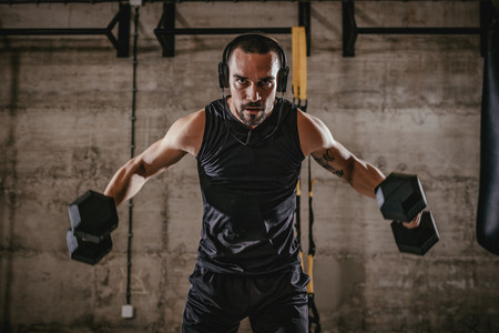 Young muscular man doing hard exercise with dumbbells for shoulders on cross fit training at the gym.の写真素材