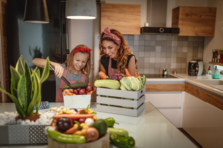Happy mother and her daughter enjoy making and having healthy meal together at their home kitchen.の写真素材