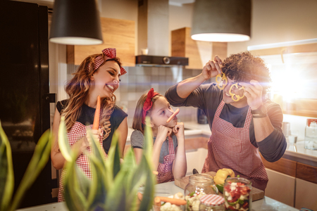Happy parents and their daughter enjoy and having fun in making and having healthy meal together at their home kitchen.の写真素材