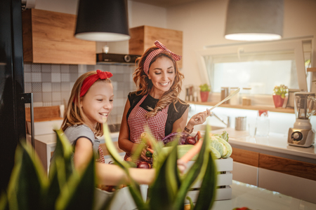 Happy mother and her daughter enjoy making and having healthy meal together at their home kitchen.の写真素材