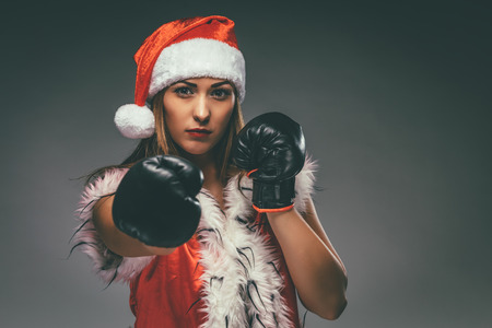 Beautiful young angry woman in Santa Claus costume with boxing gloves.の写真素材