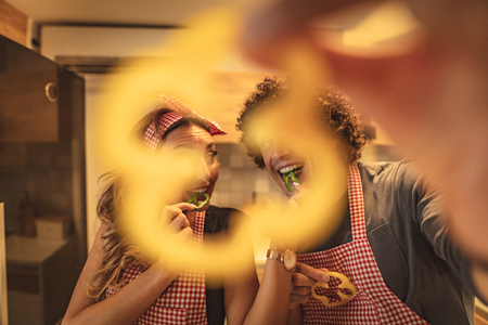 Happy young couple enjoys and having fun in eating slices of capsicum and making healthy meal together at their home kitchen.の写真素材
