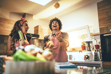 Happy young couple enjoys and having fun preparing vegetables and making healthy meal together at their home kitchen.の写真素材