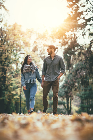 Beautiful smiling couple enjoying in sunny city park in autumn colors looking each other.の写真素材