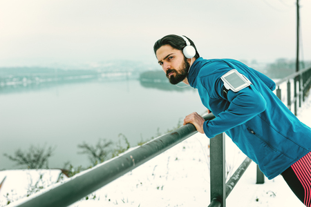 Young man athlete doing push ups and doing exercises during the winter training outside beside the river. Copy space.の写真素材