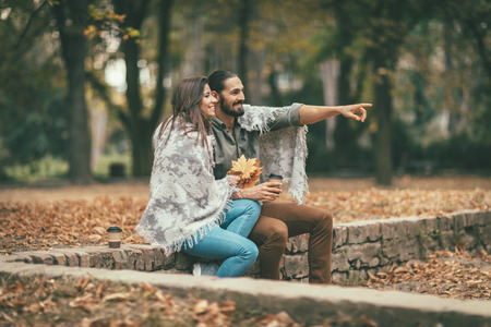 Beautiful smiling couple enjoying in sunny city park in autumn colors looking each other. They are having fun with yellow leaves.の写真素材
