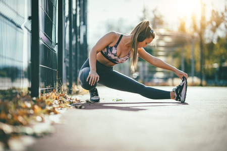 Young female runner, with headphones on her ears, doing stretching exercise on metal fence, preparing for morning workout.の写真素材
