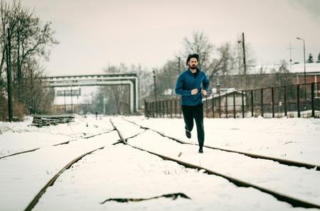 Active young man running and doing exercises across the old railroad during the winter training outside in. Copy space.の写真素材