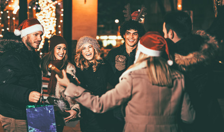 Three young cheerful couple having fun at the Christmas outdoor party in the city street at night and with a lot of lights on background.の写真素材