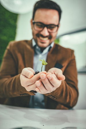 Businessman's hands are holding a fresh young plant sprout in soil. Symbol of growing and green business.の写真素材