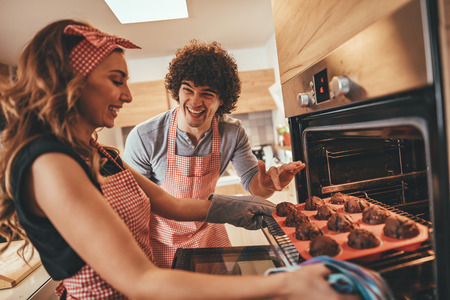 Young happy couple pulling baked muffins from the oven.の写真素材
