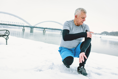 Active senior man checking mobile phone during doing exercises by the river in the winter training outside in. Copy space.の写真素材