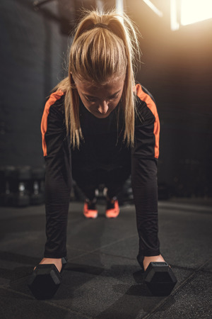 Young muscular  beautiful  woman doing push up exercise with dumbbell on hard workout at the gym.の写真素材