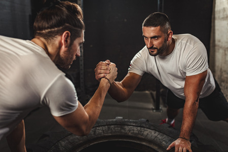 Athlete muscular sportsmen with hands clasped arm wrestling challenge between a young people.