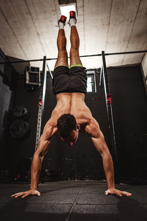 Young muscular man doing hard exercise at the gym. His is doing handstand and whole weight is on his hands.の写真素材