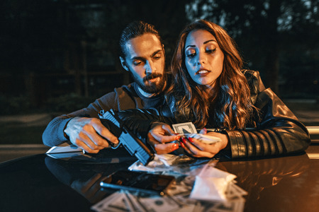 Dangerous criminal man is holding a gun and counting the money with his girlfriend after criminal...