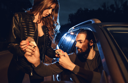 The dealer sells a little bag of heroin or cocaine to a young woman from a car, and she gives him money.の写真素材