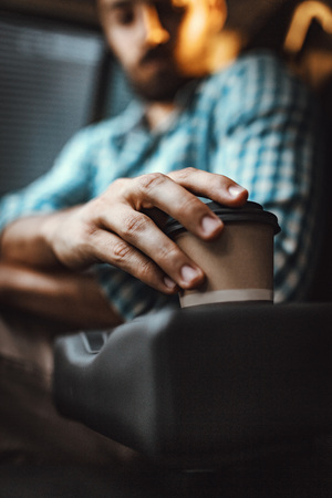 Close-up on a man's hand holding a cup of coffee, in car prepared for the trip.の写真素材