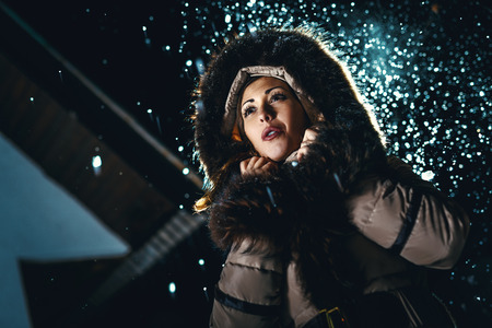 Beautiful young woman in winter jacket with fur hood worries and is looking away waiting for somebody.の写真素材
