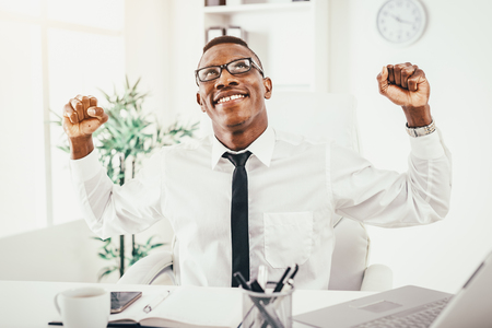 Successful African businessman celebrating success with fists in the modern office.の写真素材