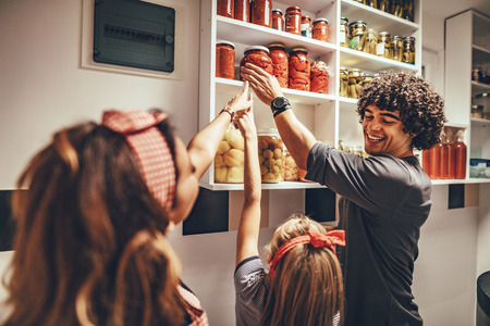 A happy family takes jars with pickled vegetables from the pantry shelf.の写真素材