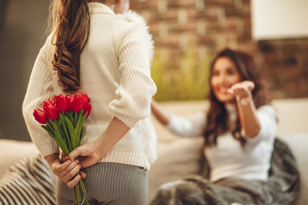 Little daughter is holding nice flowers for her amazed cheerful joyful charming mum congratulates mother's day to her.の写真素材