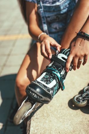 Young female skater is enjoying on the city river shore and ties her rollers on a beautiful summer day.の写真素材