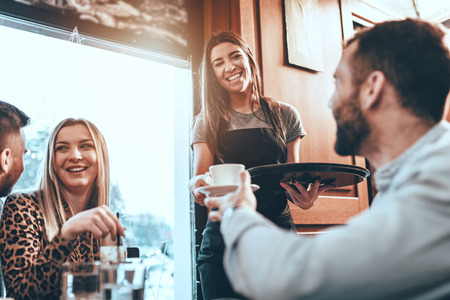 A young beautiful waitress is serving a group of young smiling friends in a cafe.の写真素材