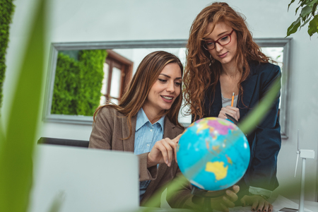 Young successful businesswomen in strategy meeting at the office are discussing new markets looking at a globe.の写真素材