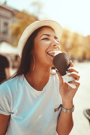 Smiling young woman with ice cream, taking break on a city square on a sunny day.の写真素材