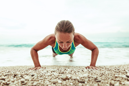 Beautiful young woman is doing push up exercises on the beach in the end of the day.の写真素材