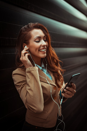 Beautiful young smiling woman listening music and holding smartphone in her hands.の写真素材