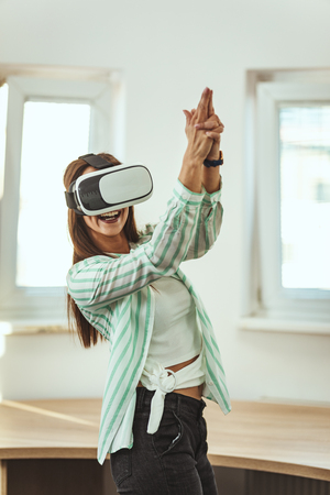 Happy young woman is playing video games with virtual reality glasses. She is having fun with new technology console online.の写真素材