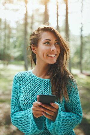 Beautiful young woman relaxing in the nature at sunny spring day and using smartphone.