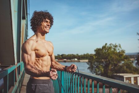 Fit muscular young man with naked torso doing exercise with resistance band on a bridge.の写真素材