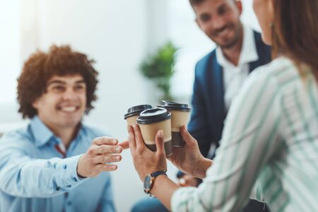 Beautiful young smiling woman with a disposable coffee cup talking on a smartphone  in the office district.の写真素材