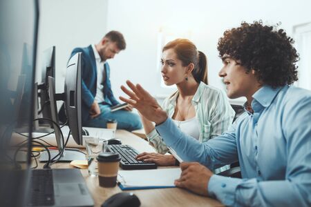 Young business people discussing some document while working on desktop computer in the casual...