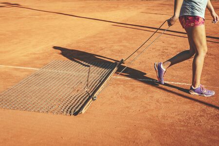 Young female tennis player harvesting red clay court to tennis match on outdoor.の写真素材