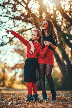 Beautiful young mother and her daughter are walking through forest. Little girl is standing beside her mother and pointing far away with finger.の写真素材